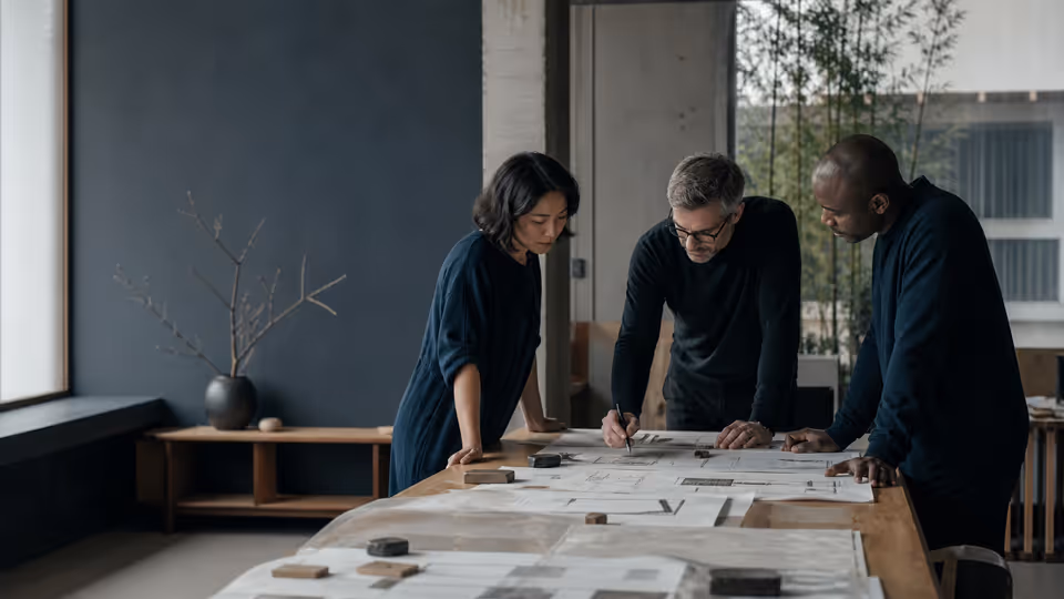 Three operations leaders studying a physical process map in a quiet design studio